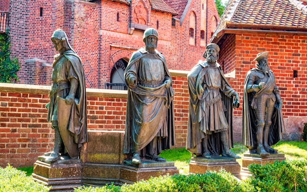 Statues of knights in front of Malbork Castle's red brick walls, Poland.