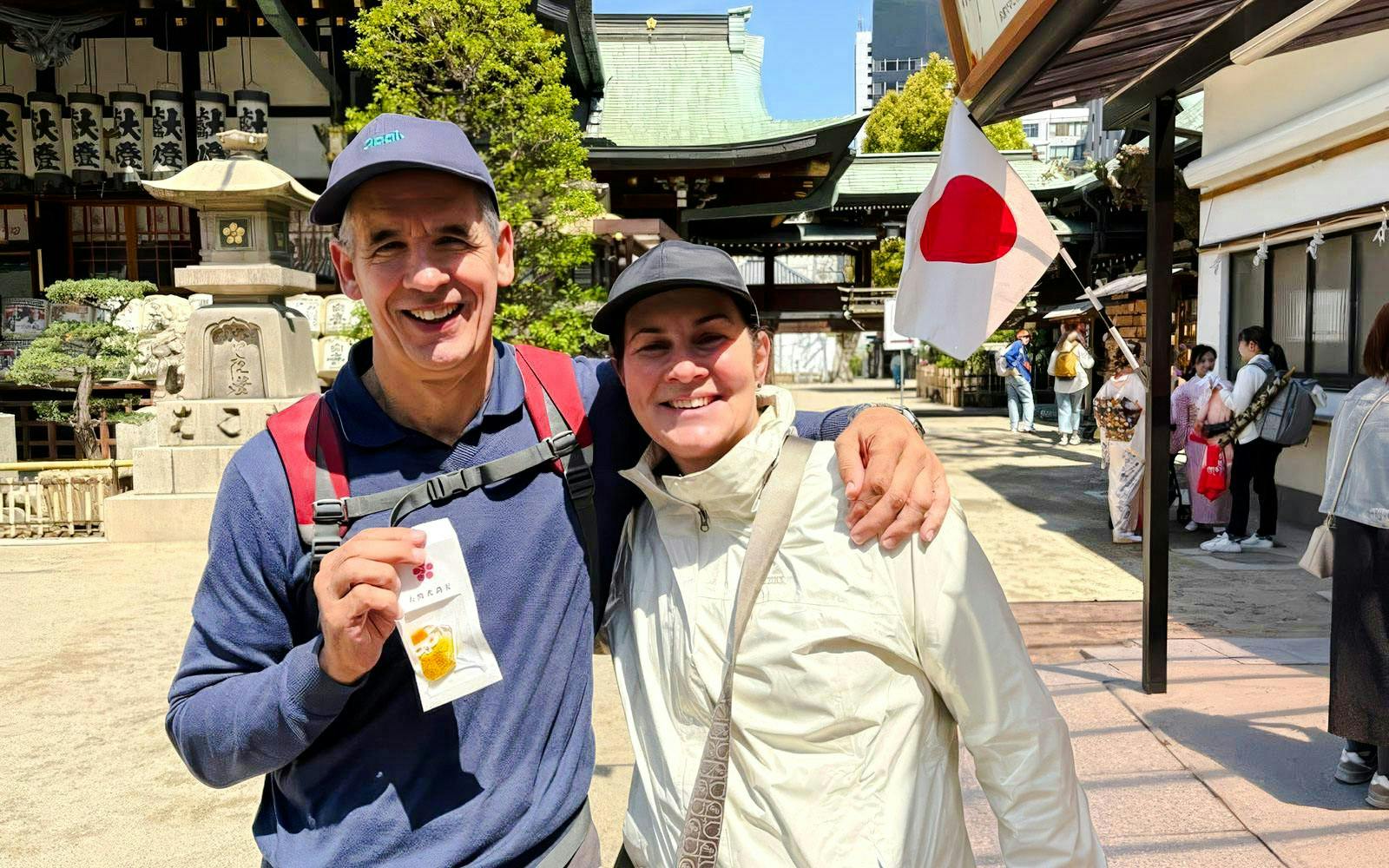 Happy couple enjoying Osaka Castle bike tour with Japanese flag in background.