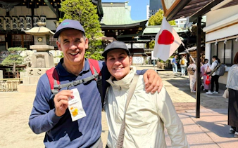 Happy couple enjoying Osaka Castle bike tour with Japanese flag in background.