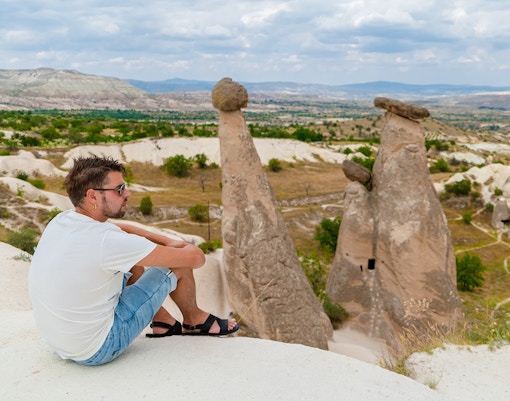 Person sitting near fairy chimneys in Pasabag Valley, Cappadocia, with scenic landscape.