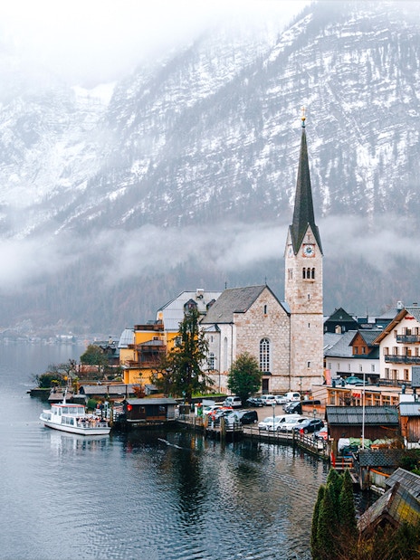 Hallstatt Church by a lake in winter, surrounded by snow-covered mountains, Austria.