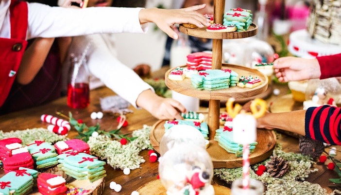 Little kids decorating Christmas cookies with icing and sprinkles on a wooden table.