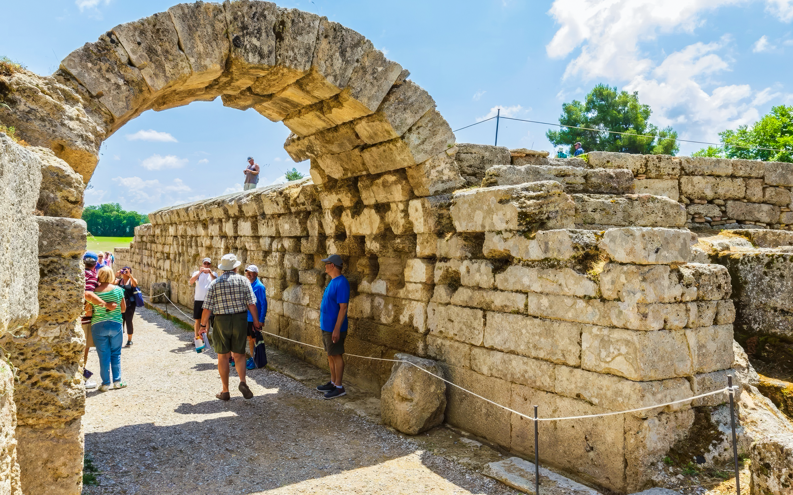 Entrance archway to ancient stadium, Olympia, Greece, with tourists exploring the site.