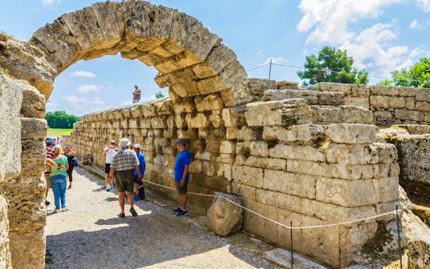 Entrance archway to ancient stadium, Olympia, Greece, with tourists exploring the site.