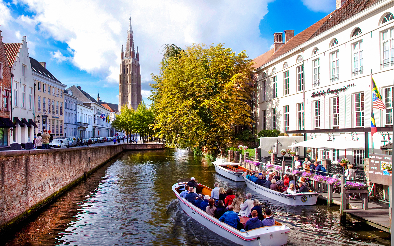 Boat tour on a canal in Bruges city center, Belgium, with historic buildings and church tower.