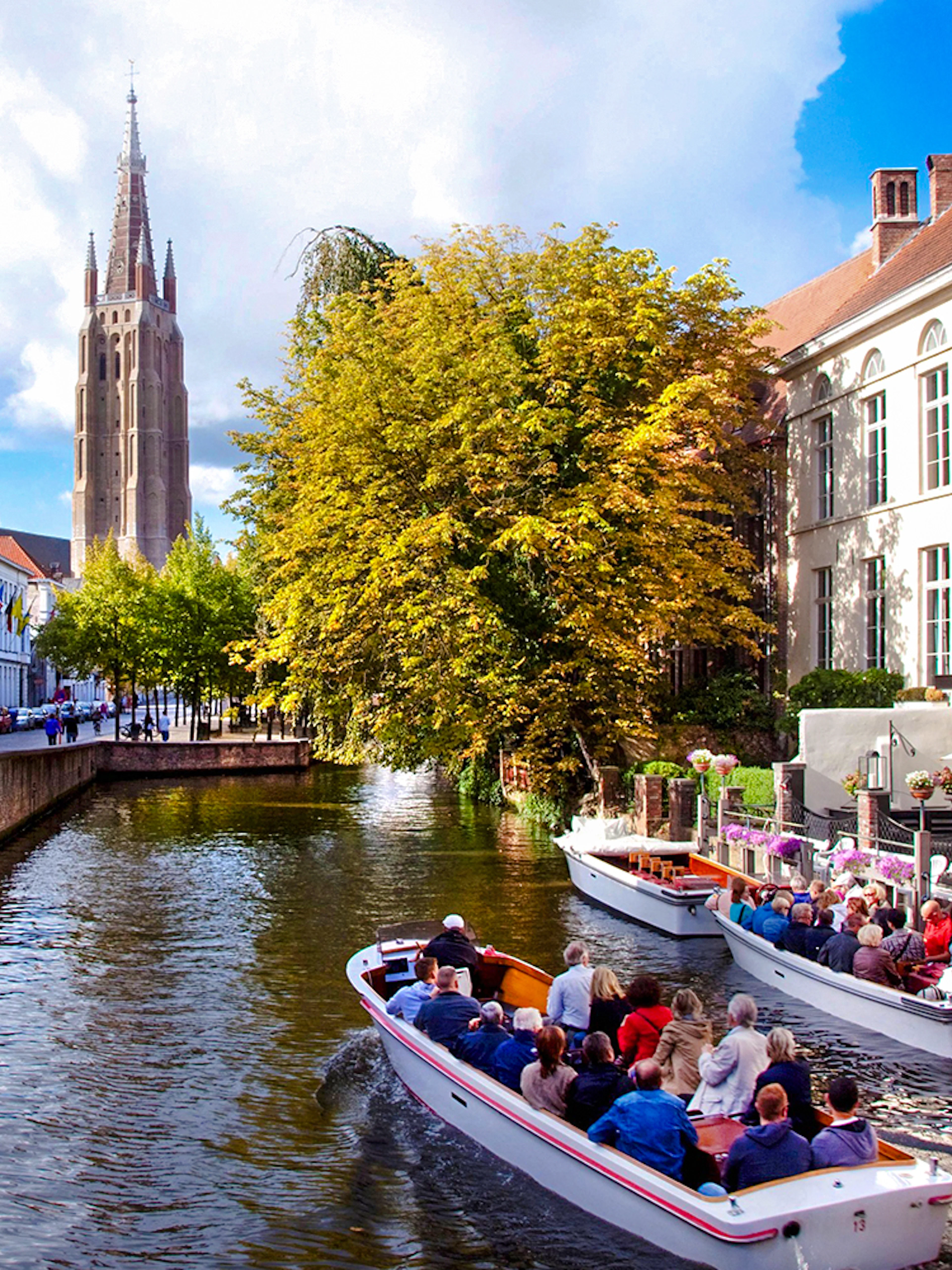 Boat tour on a canal in Bruges city center, Belgium, with historic buildings and church tower.