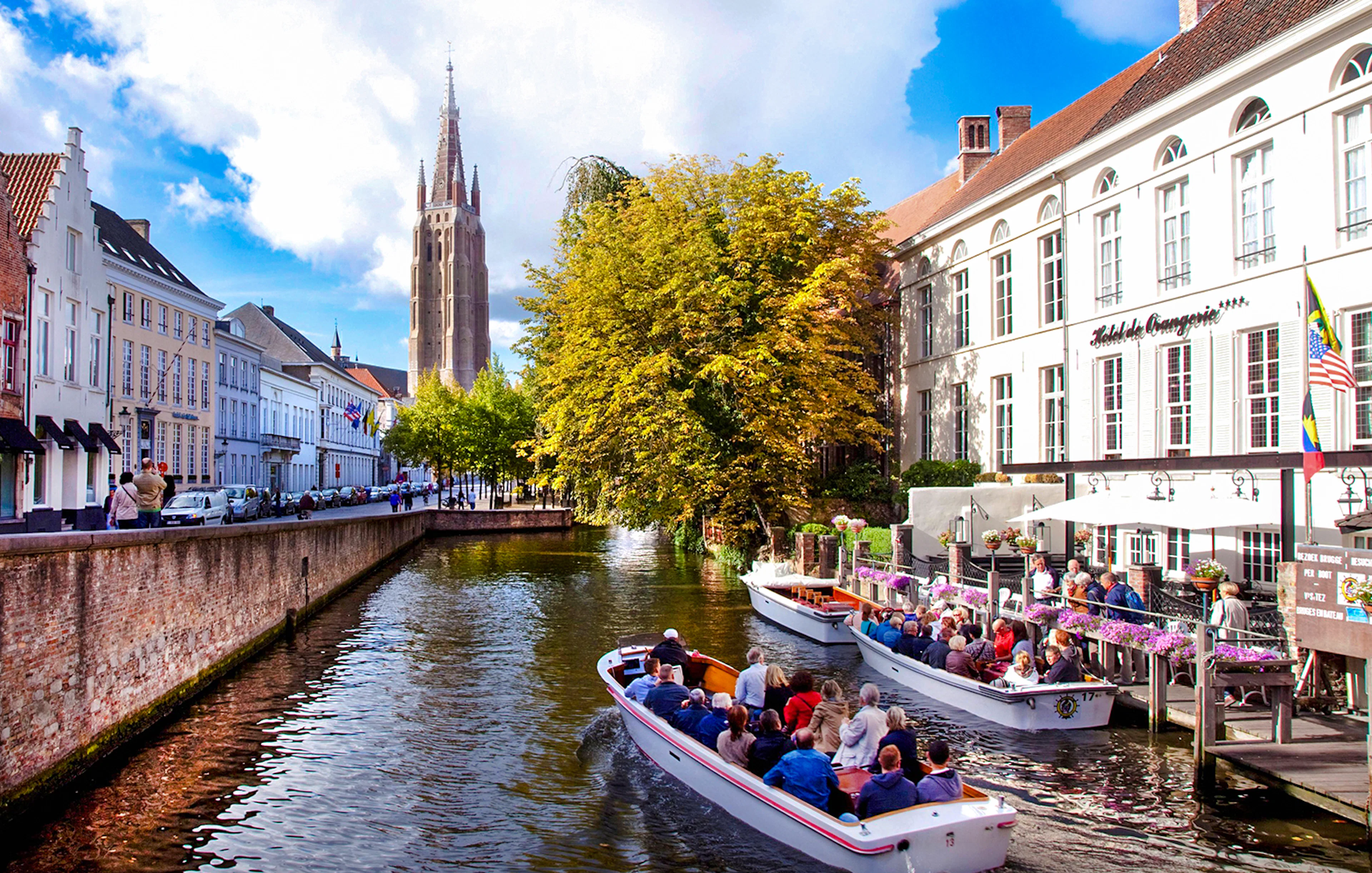 Boat tour on a canal in Bruges city center, Belgium, with historic buildings and church tower.