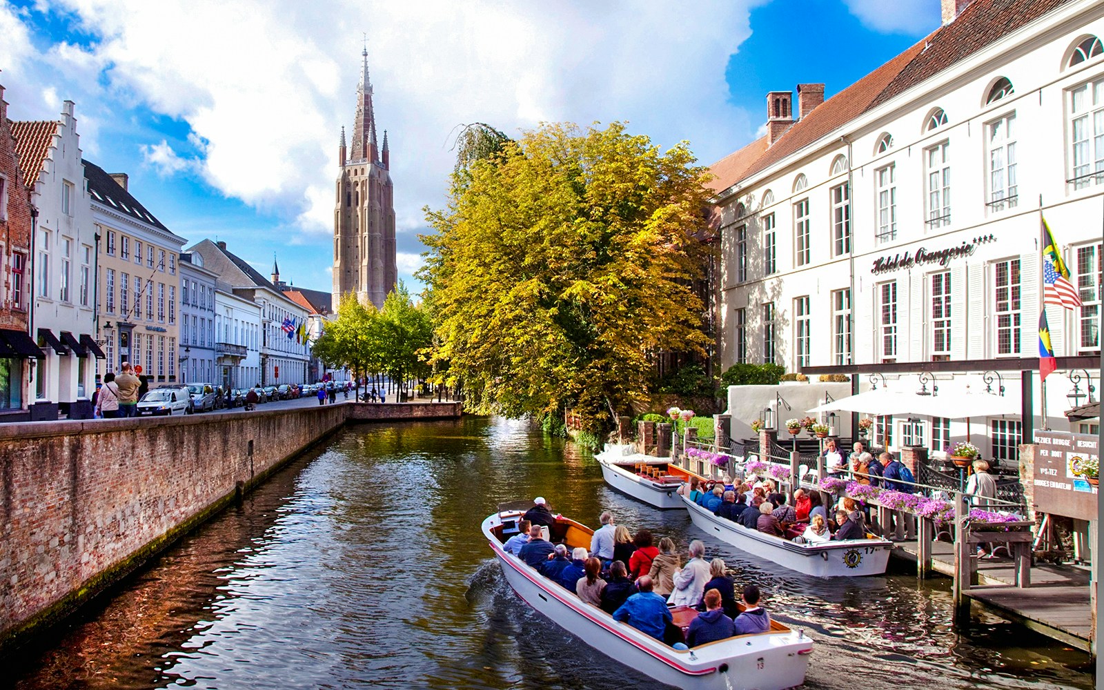 Boat tour on a canal in Bruges city center, Belgium, with historic buildings and church tower.