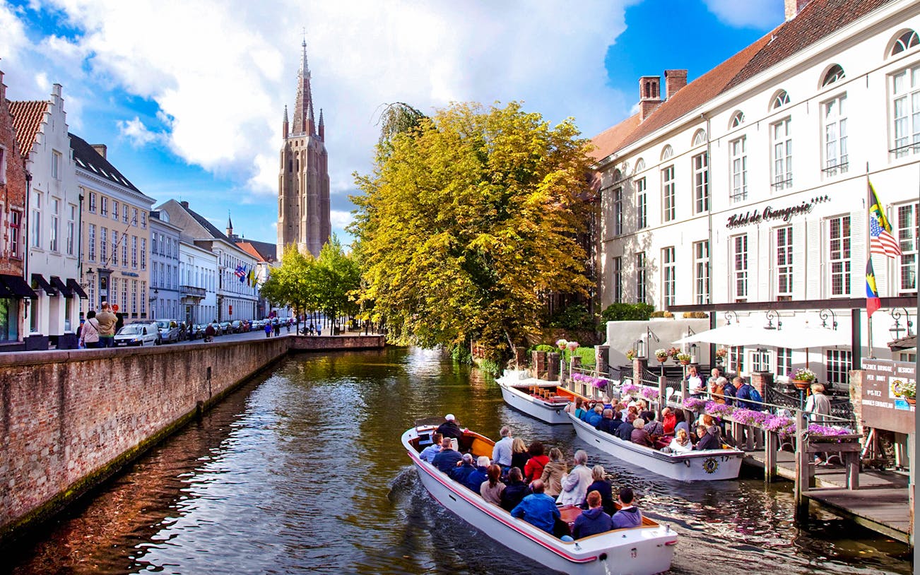 Boat tour on a canal in Bruges city center, Belgium, with historic buildings and church tower.