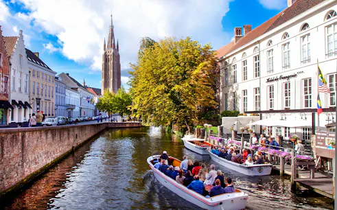 Boat tour on a canal in Bruges city center, Belgium, with historic buildings and church tower.