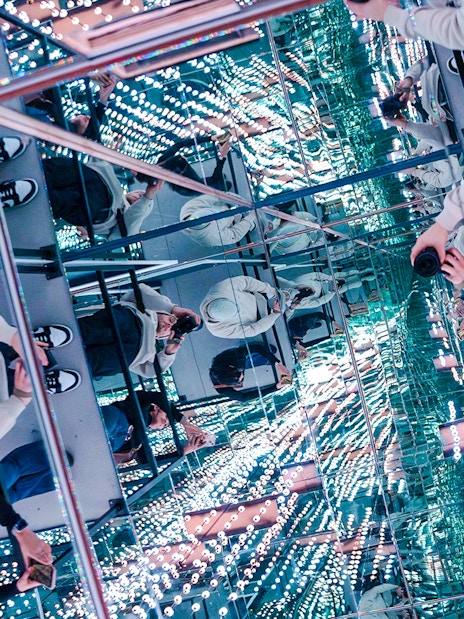 Guests exploring mirrored room at World Of Illusions with reflections and lights.