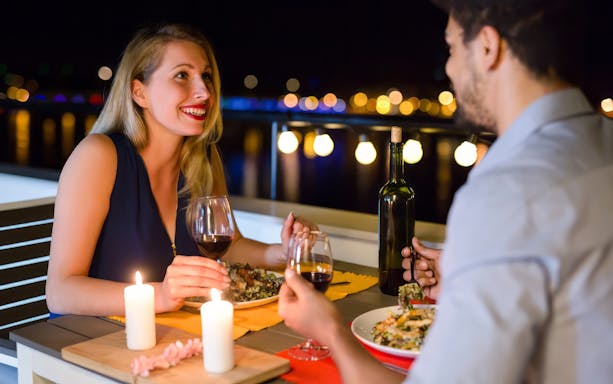 Couple enjoying dinner on a romantic cruise in Paris with wine and candlelight.