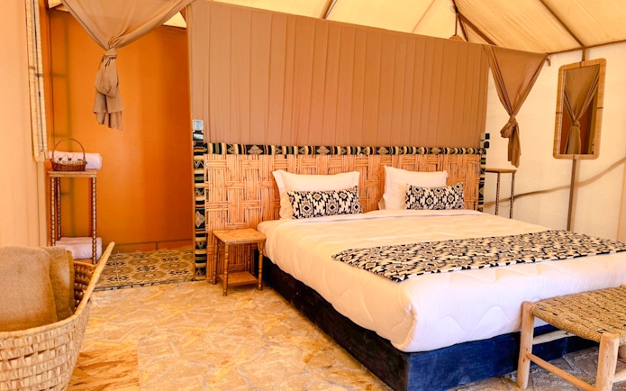 Interior view of a Marrakech desert camp tent with a bed, woven headboard, and patterned decor.