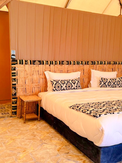 Interior view of a Marrakech desert camp tent with a bed, woven headboard, and patterned decor.