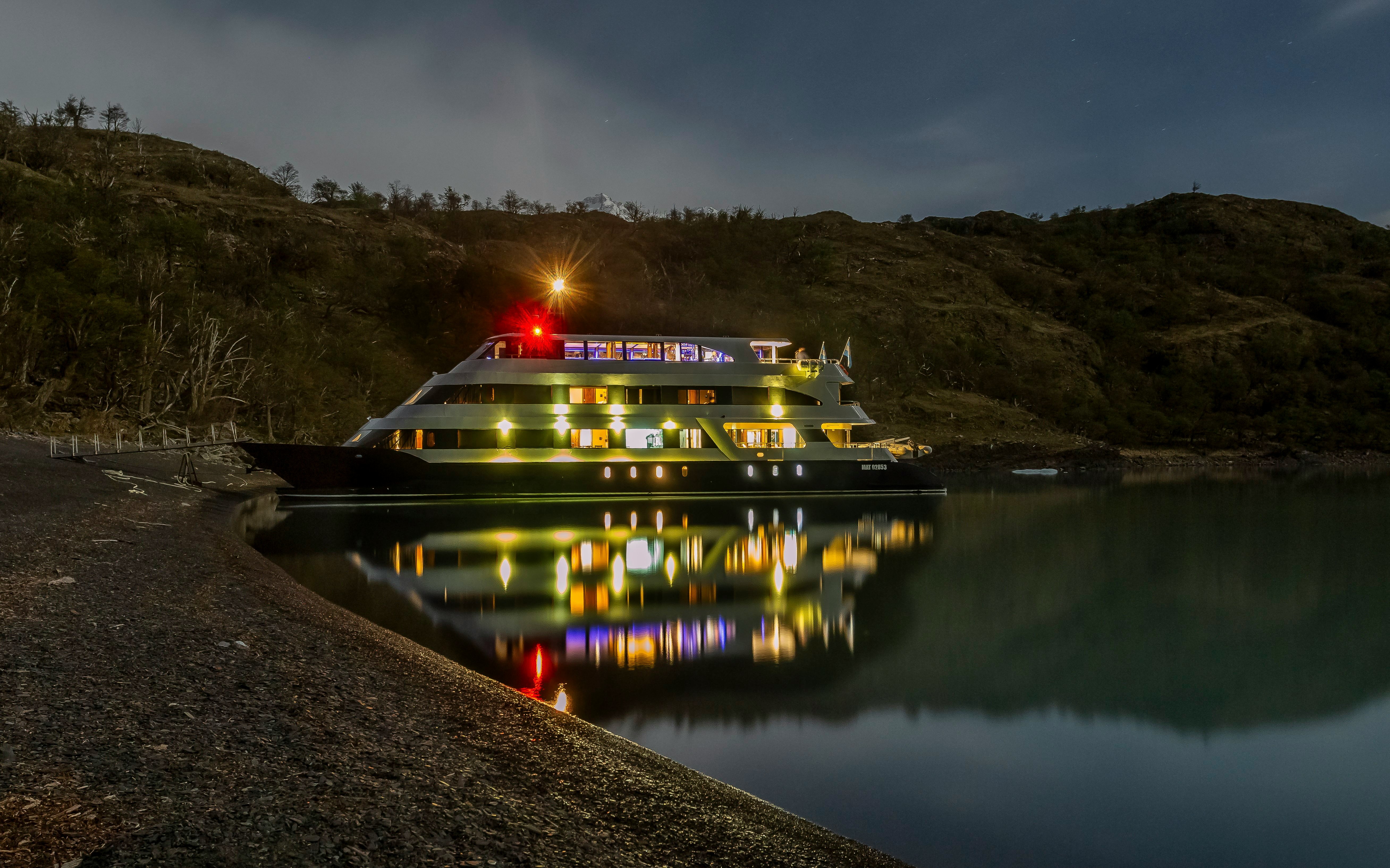 Night cruise ship docked at Perito Moreno during dusk, reflecting on calm water.