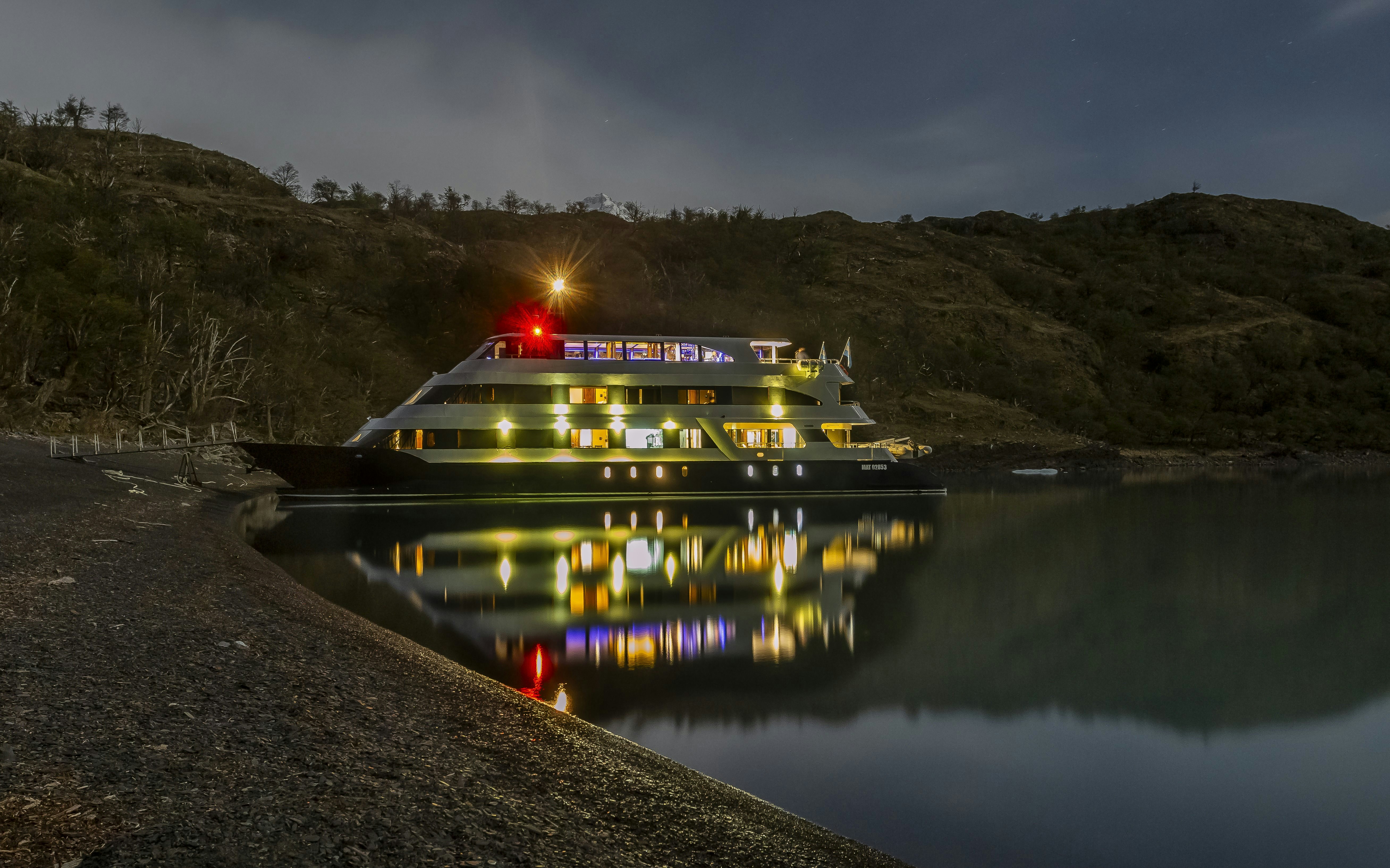 Night cruise ship docked at Perito Moreno during dusk, reflecting on calm water.