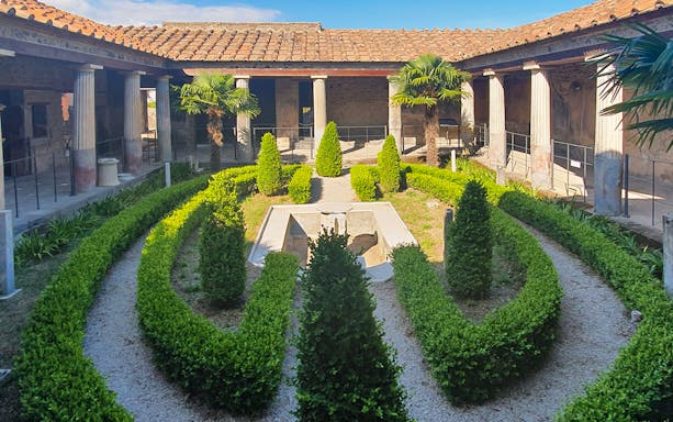 Pompeii courtyard with manicured hedges and ancient columns on a guided tour.