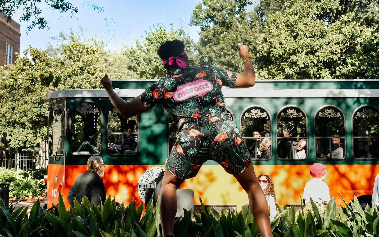 Person in colorful outfit dancing in front of Savannah trolley with passengers.