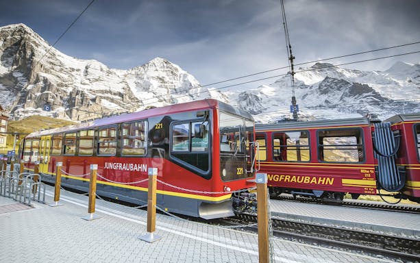 Jungfraubahn train at station with snowy Eiger mountain backdrop, Switzerland.