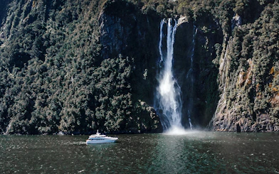 Cruise boat near waterfall in Milford Sound, New Zealand.