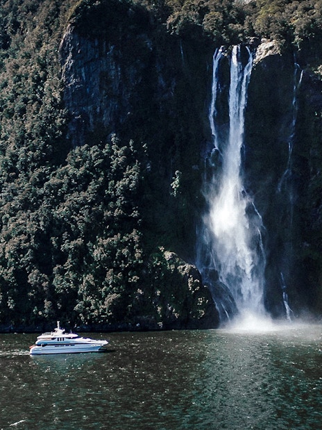 Cruise boat near waterfall in Milford Sound, New Zealand.