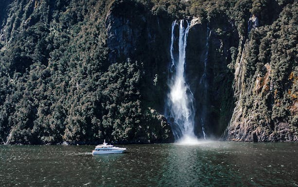 Cruise boat near waterfall in Milford Sound, New Zealand.