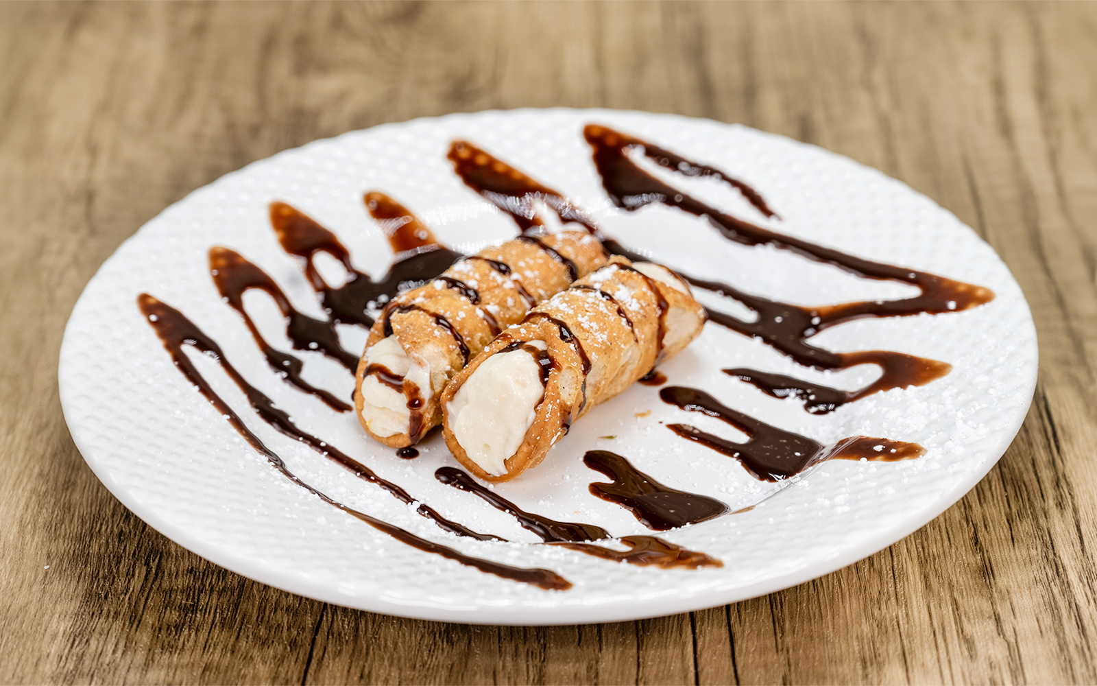 Cannoli with chocolate syrup on a white plate, traditional Italian dessert.