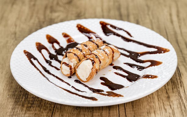 Cannoli with chocolate syrup on a white plate, traditional Italian dessert.