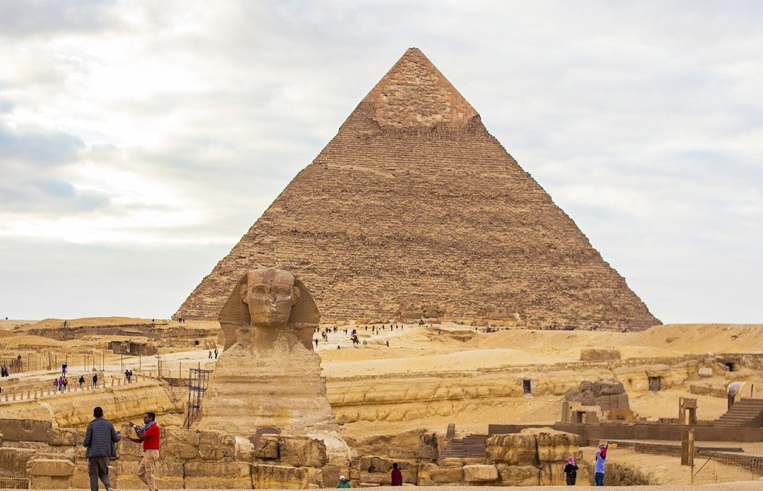 Great Sphinx and Pyramid of Khafre in Giza, Egypt, with tourists exploring the site.