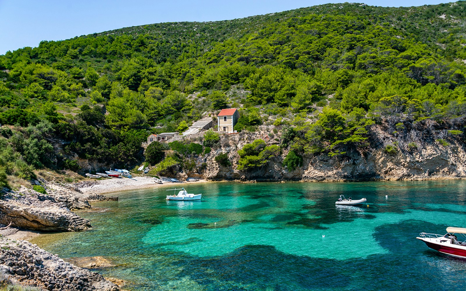 Boats anchored in a clear bay with lush greenery on Biševo Island, Adriatic Sea.