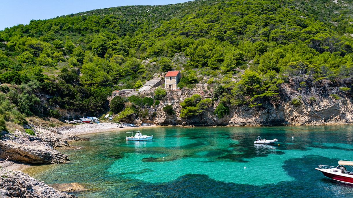 Boats anchored in a clear bay with lush greenery on Biševo Island, Adriatic Sea.