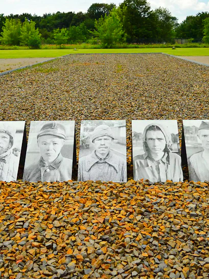 Memorial photos of prisoners at Sachsenhausen Concentration Camp, Germany, with gravel path and trees.