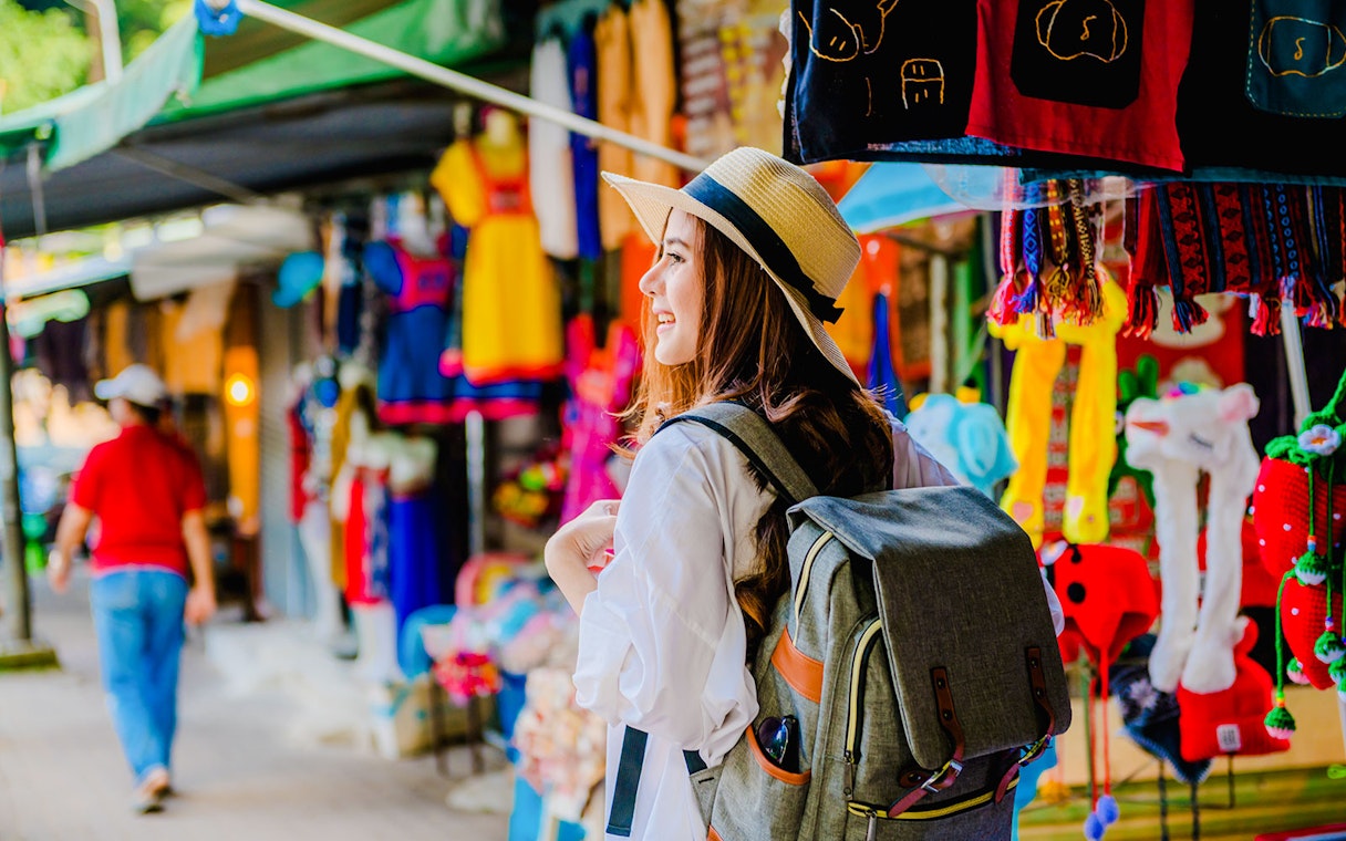 Girl with backpack exploring vibrant market stalls in Doi Suthep, Thailand.