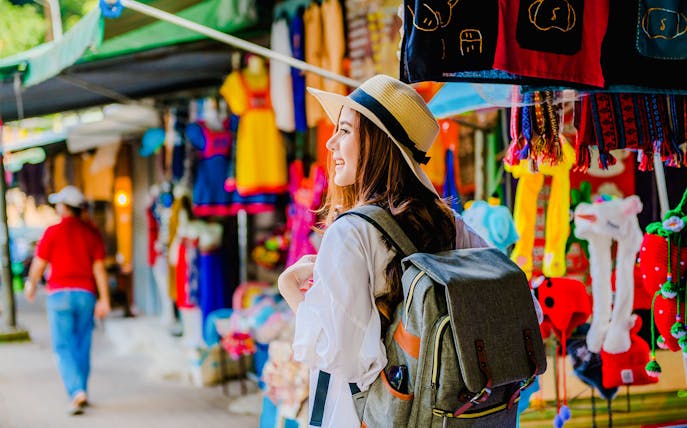 Girl with backpack exploring vibrant market stalls in Doi Suthep, Thailand.