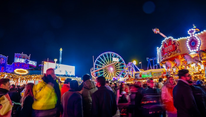 People walking at night in Hyde Park's Winter Wonderland, London, with colorful rides and attractions.