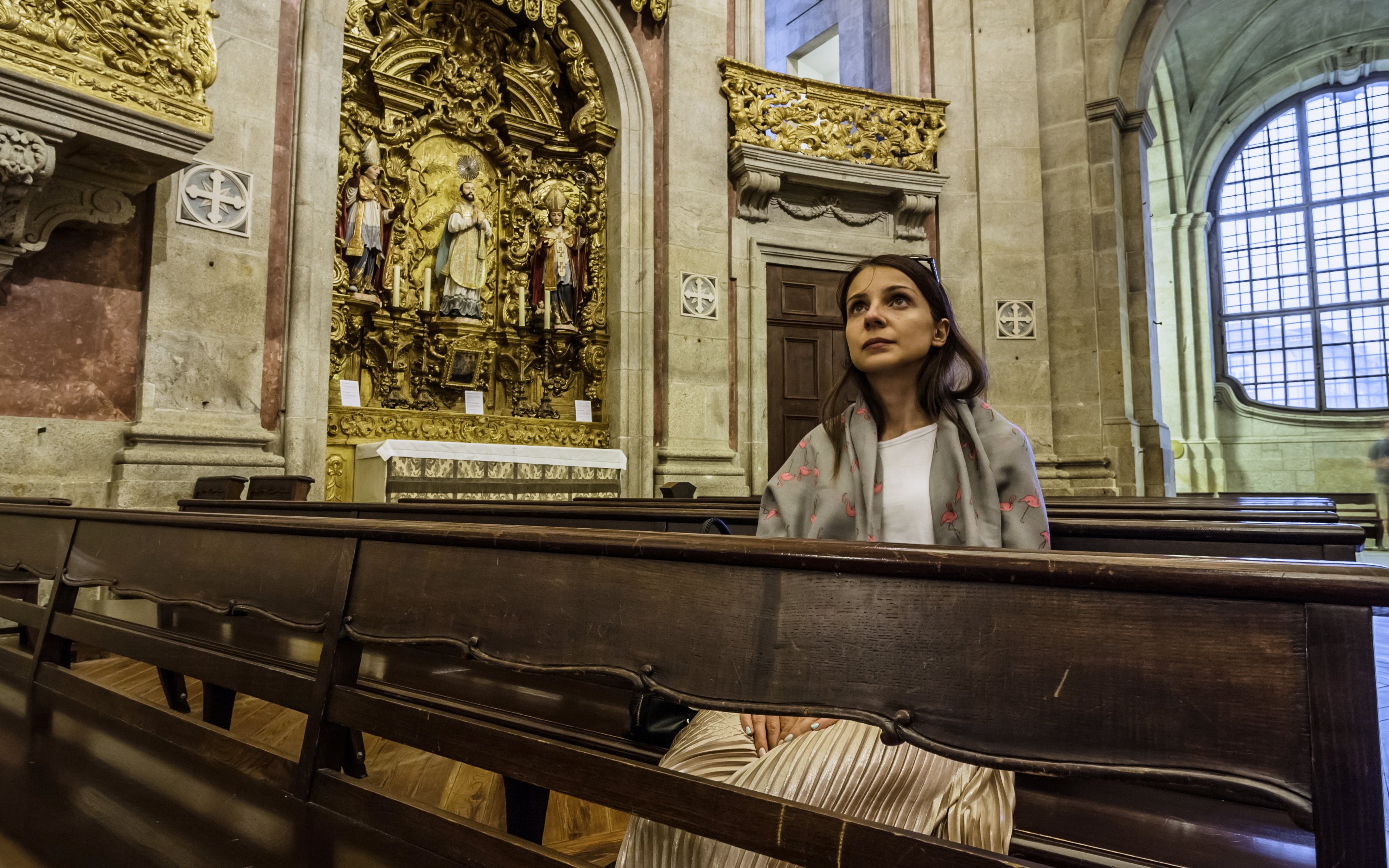 Girl praying in Clerigos Church, Porto, seated in pews near ornate altar.