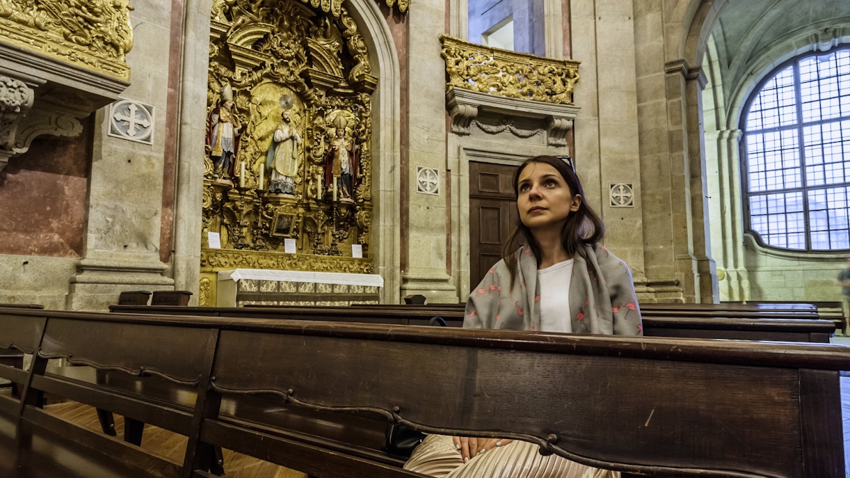 Girl praying in Clerigos Church, Porto, seated in pews near ornate altar.