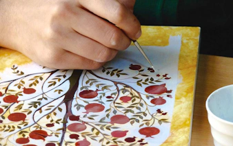 Local artisan painting pomegranate design at pottery workshop in Baku.