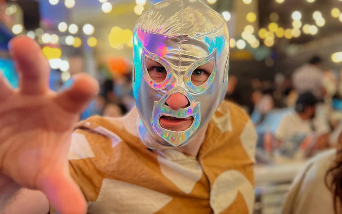 Luchador in silver mask reaching forward at Lucha Libre & Michelada Workshop.