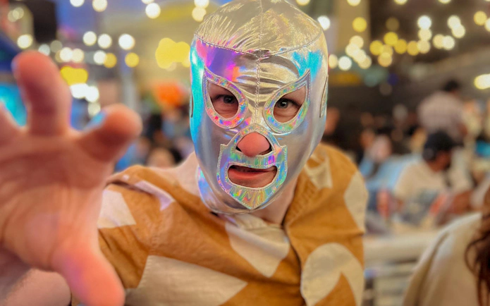Luchador in silver mask reaching forward at Lucha Libre & Michelada Workshop.