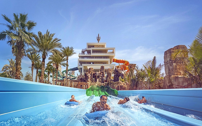 Visitors enjoying waterslides at Aquaventure Waterpark, Dubai, with palm trees and a tower in the background.
