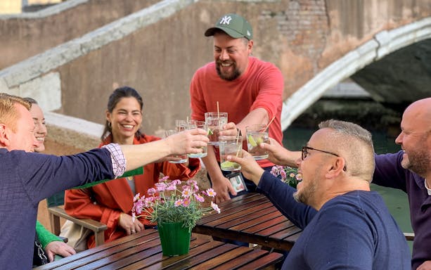 Group enjoying drinks by a canal in Venice on the Ultimate Spritz Tour.