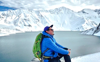 Man sitting by Embalse del Yeso with snowy Andes mountains in Cajón del Maipo, Santiago.