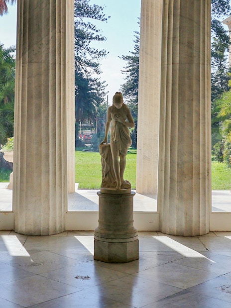 Statues inside Villa Pignatelli, Naples, with garden view through columns.