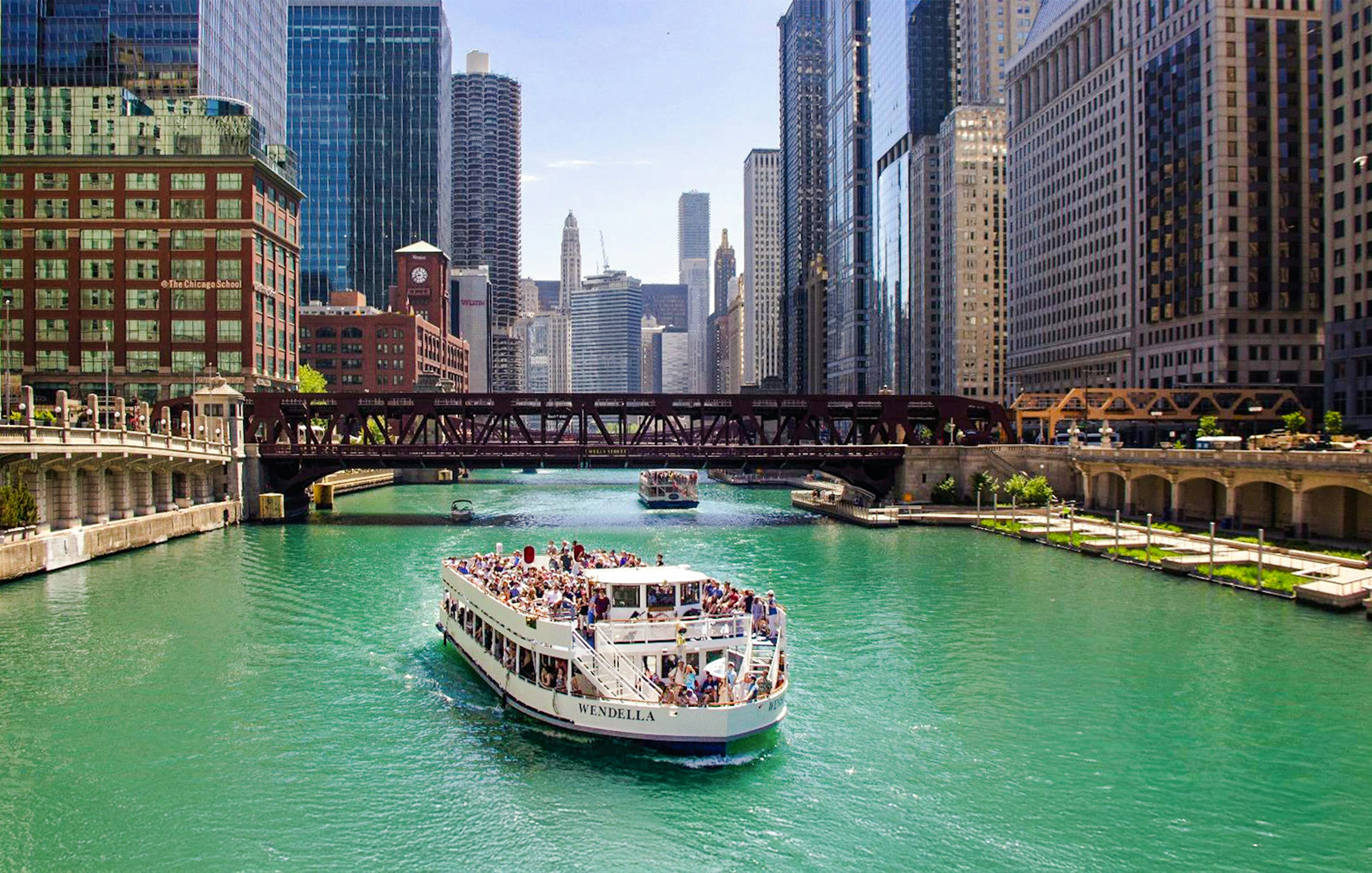 Chicago River cruise boat passing under a bridge with city skyline.