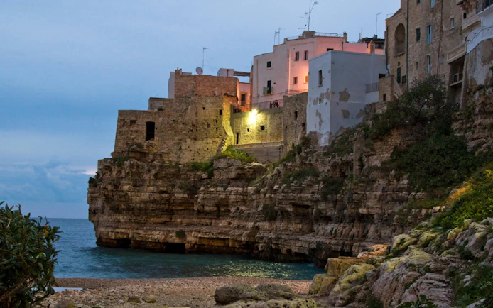 Cliffside buildings in Polignano a Mare at dusk, Valle d'Itria tour from Bari.
