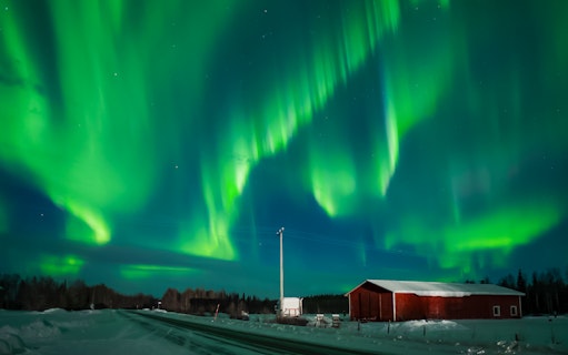 Northern Lights over snowy landscape with red cabin in Levi, Finland.