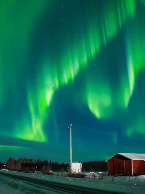 Northern Lights over snowy landscape with red cabin in Levi, Finland.