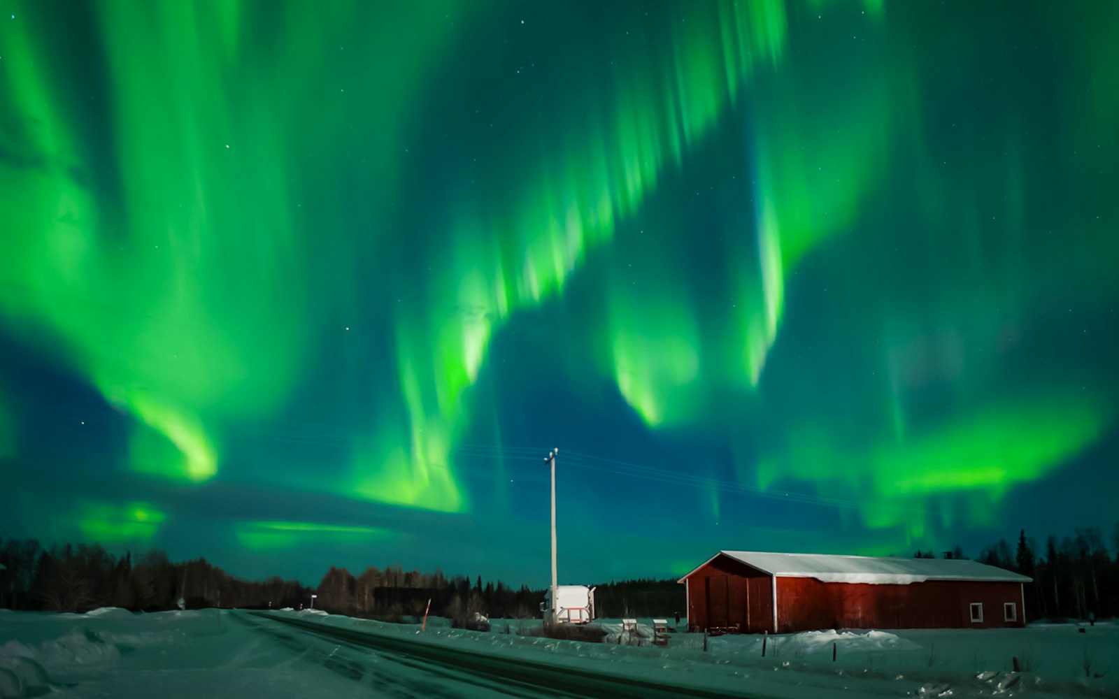 Northern Lights over snowy landscape with red cabin in Levi, Finland.