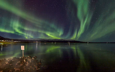 Northern Lights over a calm lake with distant snowy mountains in Iceland.